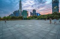 a woman is walking in the foreground of an empty city square at dusk with skyscrapers in the background