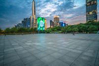 a woman is walking in the foreground of an empty city square at dusk with skyscrapers in the background