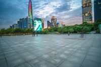 a woman is walking in the foreground of an empty city square at dusk with skyscrapers in the background