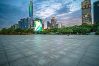 a woman is walking in the foreground of an empty city square at dusk with skyscrapers in the background