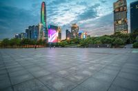 a woman is walking in the foreground of an empty city square at dusk with skyscrapers in the background