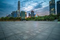 a woman is walking in the foreground of an empty city square at dusk with skyscrapers in the background