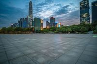 a woman is walking in the foreground of an empty city square at dusk with skyscrapers in the background