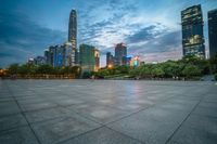 a woman is walking in the foreground of an empty city square at dusk with skyscrapers in the background