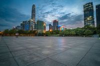 a woman is walking in the foreground of an empty city square at dusk with skyscrapers in the background