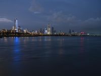 a skyline view of a city at night reflected in the water of lake michigan, with light - up buildings