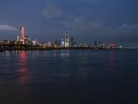 a skyline view of a city at night reflected in the water of lake michigan, with light - up buildings