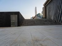 the stairs are leading into a building and a large skyscraper rises in the distance over the stairs