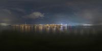 the night sky with clouds and a city lights reflected on a body of water with a lighthouse in the middle