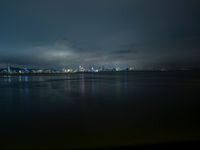 a lake with lights on the waterfront and a boat in the water at night on a cloudy day