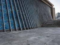 a person walking on the pavement in front of a tall building with stairs down the middle