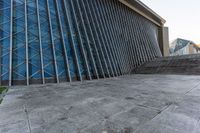 a person walking on the pavement in front of a tall building with stairs down the middle