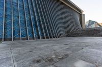 a person walking on the pavement in front of a tall building with stairs down the middle