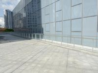the empty tiled walkway is lined with glass windows and a metal railing to allow pedestrians in the area