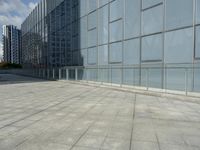 the empty tiled walkway is lined with glass windows and a metal railing to allow pedestrians in the area