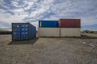 several blue, orange and white shipping containers next to each other in an area where dirt and some grass