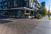 a person walks down a brick walkway in front of an apartment complex with an awning,