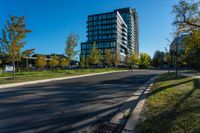 there is a tall building that sits near the road in front of it, and has many trees