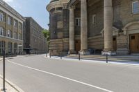 a long sidewalk in front of a building that has columns and columns behind it, along with a bench