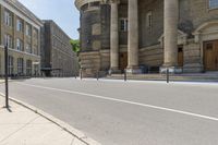 a long sidewalk in front of a building that has columns and columns behind it, along with a bench