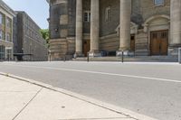 a long sidewalk in front of a building that has columns and columns behind it, along with a bench