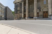 a long sidewalk in front of a building that has columns and columns behind it, along with a bench