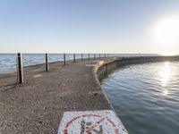 a sidewalk leading to an empty body of water next to the ocean with chains on it