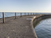 a sidewalk leading to an empty body of water next to the ocean with chains on it