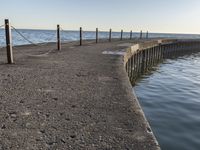 a sidewalk leading to an empty body of water next to the ocean with chains on it