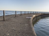 a sidewalk leading to an empty body of water next to the ocean with chains on it