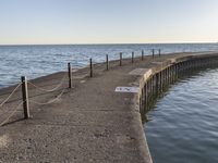 a sidewalk leading to an empty body of water next to the ocean with chains on it