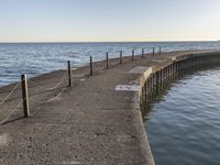 a sidewalk leading to an empty body of water next to the ocean with chains on it