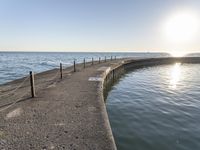 a sidewalk leading to an empty body of water next to the ocean with chains on it