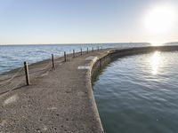 a sidewalk leading to an empty body of water next to the ocean with chains on it