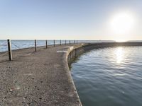 a sidewalk leading to an empty body of water next to the ocean with chains on it