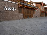 people walk on a sidewalk next to a stone building with chinese writing and decorations on it