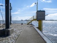 a sidewalk and walkway near the water by a large building with stairs and metal poles