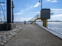 a sidewalk and walkway near the water by a large building with stairs and metal poles