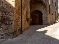 a street with two doors and flower pots on the walls in the city of siena