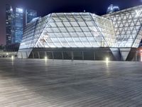 a modern building in the city at night with its lit up lights on and walkway