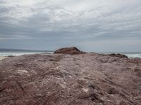 a person is sitting on the edge of a rocky ledge at the beach with the ocean behind him