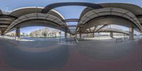 a large skate park with multiple ramps and benches, under a freeway bridge with an overpass