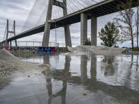 skate park with a long bridge above it in a cloudy sky, reflecting the water and graffiti on the concrete