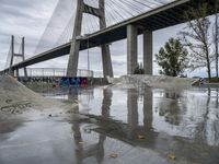 skate park with a long bridge above it in a cloudy sky, reflecting the water and graffiti on the concrete