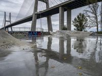 skate park with a long bridge above it in a cloudy sky, reflecting the water and graffiti on the concrete