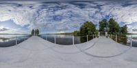 the 360 - view of a skate park on a calm lake shore surrounded by trees