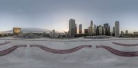 a skate boarder jumping on a ramp at the top of a skate park with some high rise buildings behind them