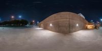 a skate park with the lights turned on at night and people walking around the parking lot