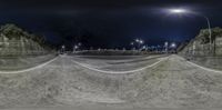 a skate park at night with a bike ramp to the right and lights on in the distance