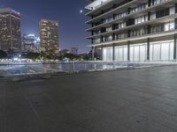 a skate board sitting on top of a concrete floor near tall buildings at night as seen from a sidewalk